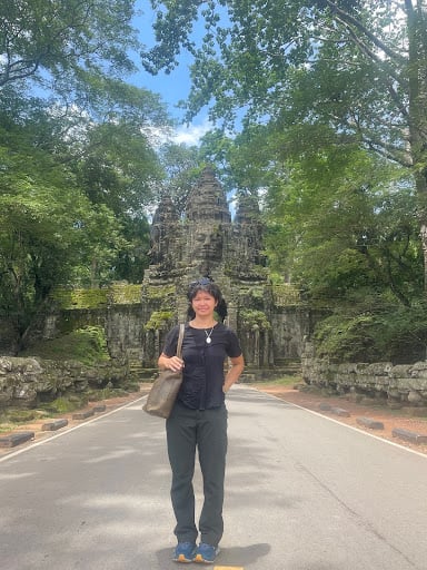 Person standing in front of temple with greenery.